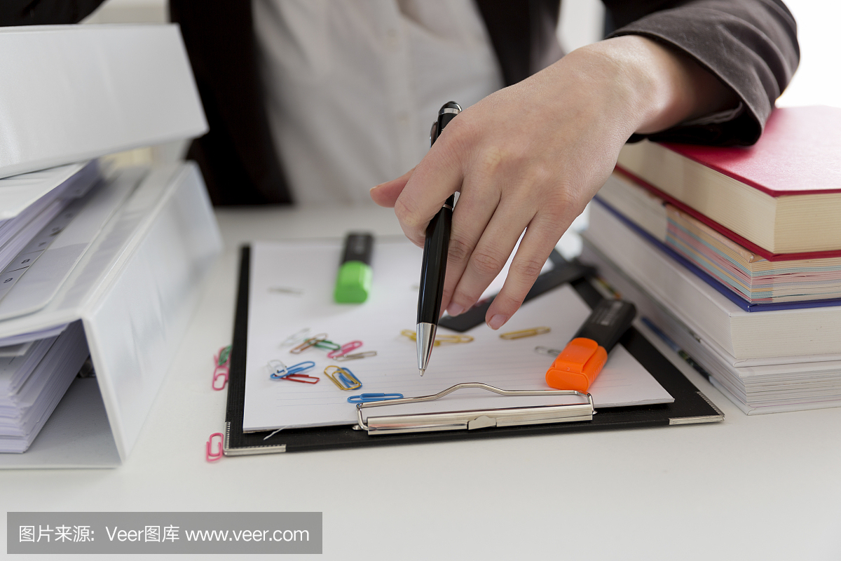 坐在滿是文書,書籍和文件的桌子旁的女人。混亂的工作場所。過載和過度勞累